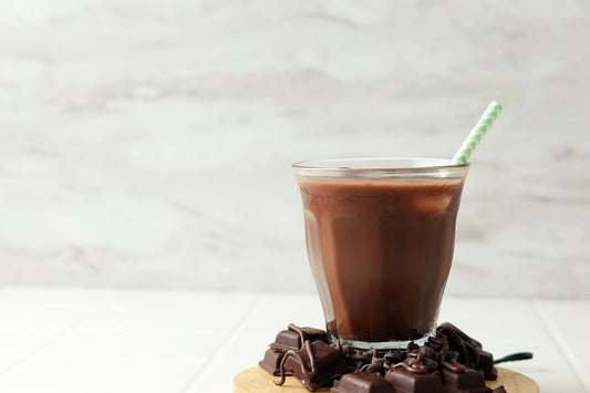 Glass of iced drinking chocolate with dark chocolate chunks on a wooden coaster, showing the rich and refreshing side of The Gentle Mug blend