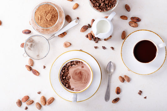 Two mugs of rich drinking chocolate surrounded by cocoa beans, powder, and milk – showcasing the difference between drinking chocolate and hot chocolate.