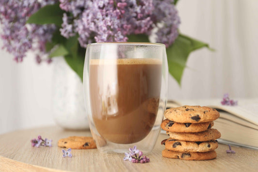 Double-walled glass of rich hot chocolate with chocolate chip cookies and lilac flowers, capturing the indulgent ritual of luxury cocoa